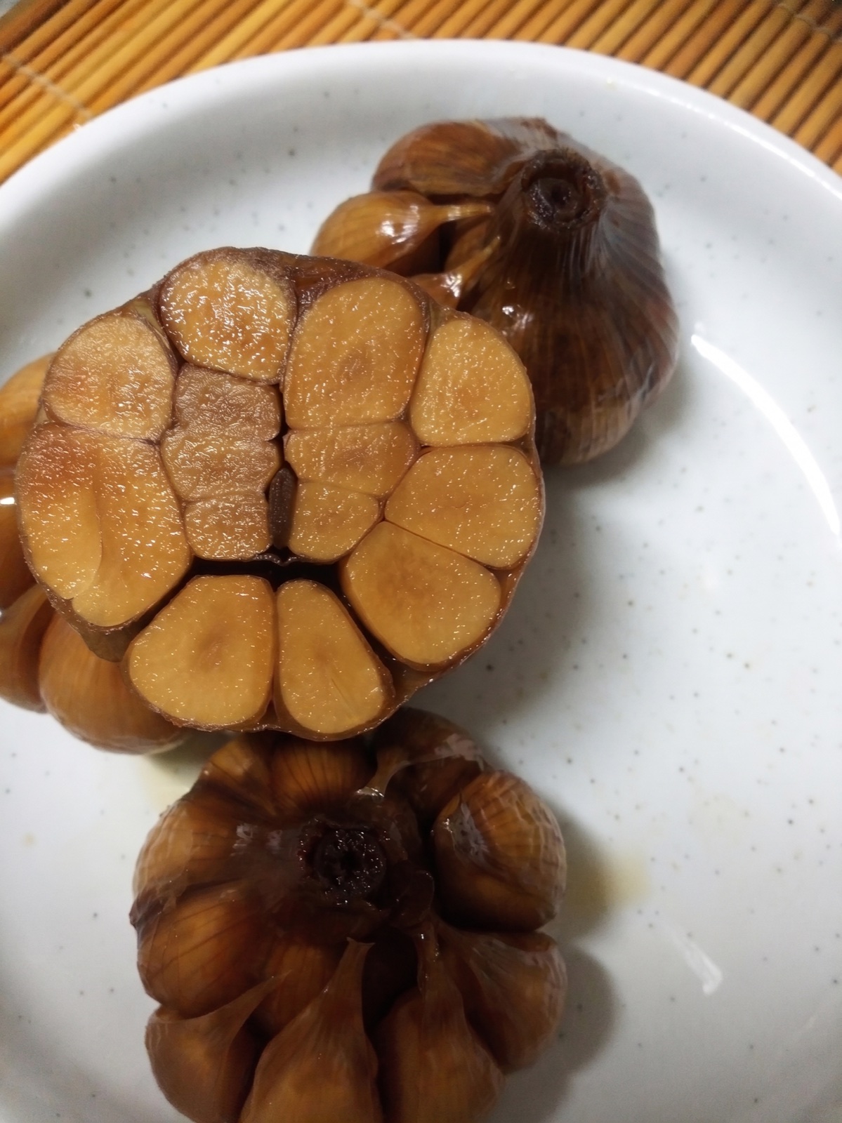 Maneul jangajji — whole heads of Korean garlic pickled in soy sauce and vinegar, one cut in half to show the amber-colored cloves inside, on a white plate