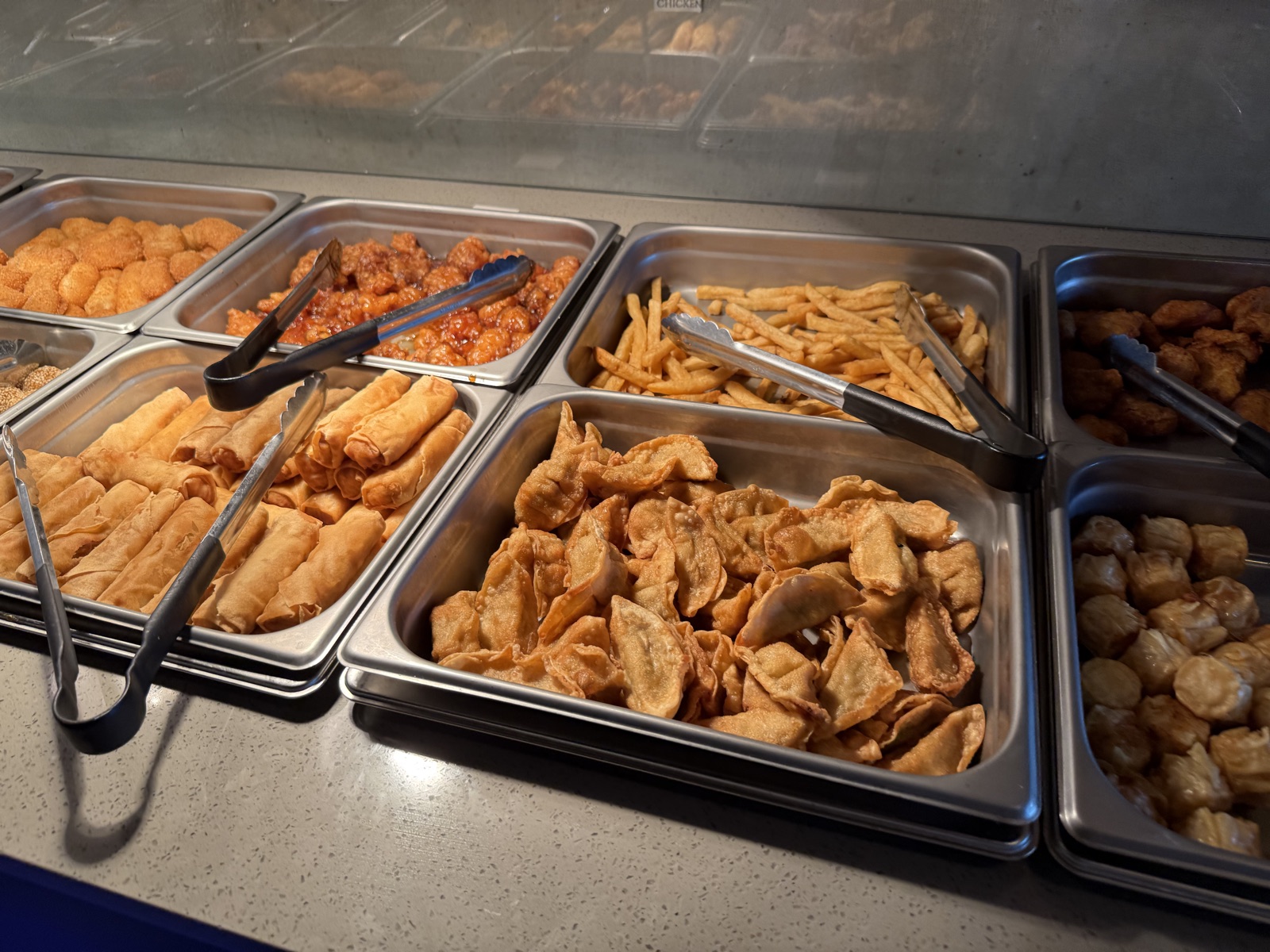 Steam trays on the hot food bar at Sushi Oishii holding fried dumplings, egg rolls, french fries and popcorn chicken